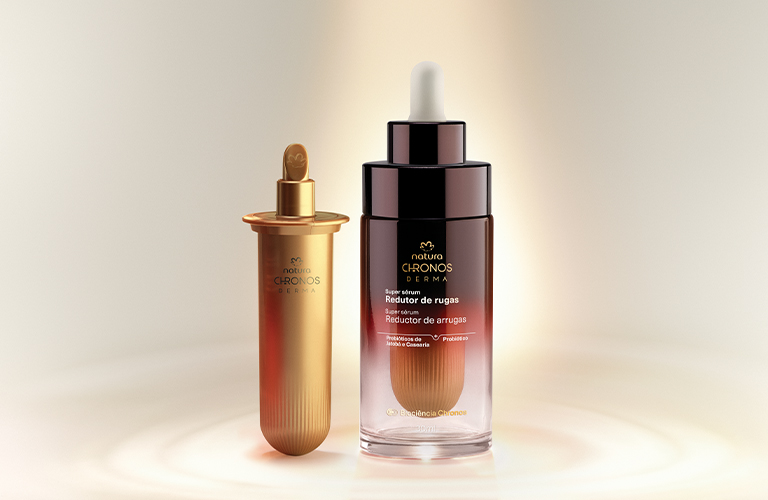 Foto de una gota de sérum o producto cosmético de color beige claro formándose en la punta de un aplicador, sobre un fondo blanco.